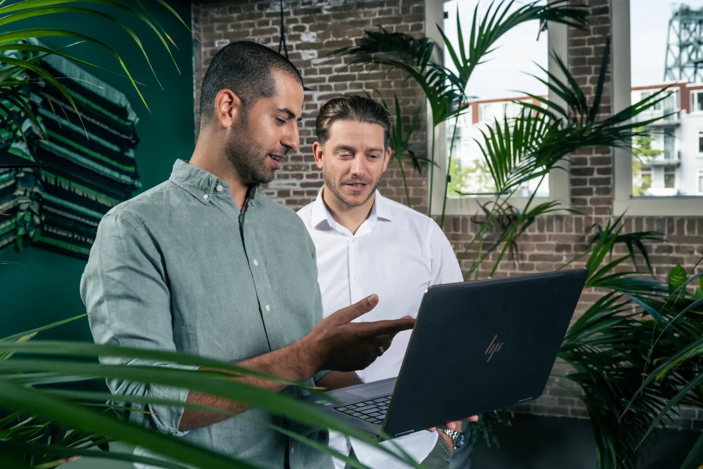 Twee mannen bekijken samen een laptop in een kantoor met veel planten